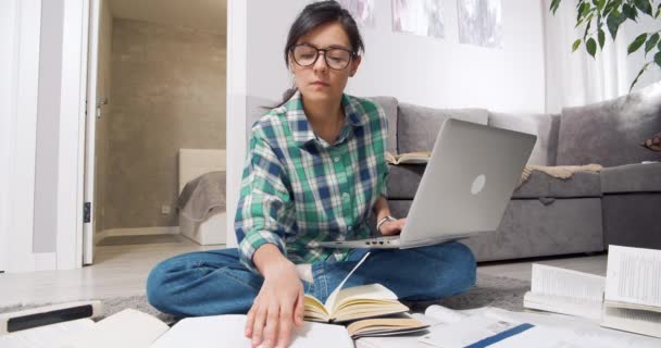 Concentrado jovem estudante ou jornalista com óculos à procura de informações em muitos livros e livros didáticos e digitar algo em um laptop em casa. Conceito de educação — Vídeo de Stock