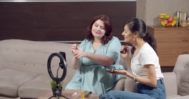 Két fiatal nő teszteli kozmetikai highlighter kéznél, miközben rögzíti videó vagy élő stream okostelefon otthon. Szépség, blogolás és közösségi média koncepció — Stock videók