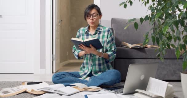 Giovane studentessa stanca mettendo da parte il libro, togliendosi gli occhiali e chiudendo il portatile rilassandosi dopo un duro lavoro a casa o la preparazione dell'esame — Video Stock