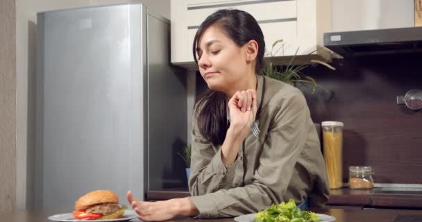 Karcsú fiatal nő elteszi tányér burger és mosolygós eszik zöld zöldség saláta a konyhában. Vegarianizmus, étrend és egészséges táplálkozás — Stock videók