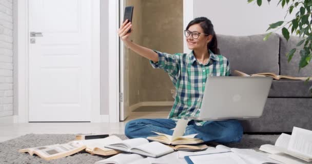 Mulher sorrindo usando óculos tirando selfie ou gravando vídeo usando smartphone enquanto estuda ou trabalha remotamente em casa — Vídeo de Stock