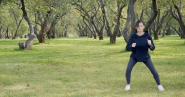 Spor giyimli genç ve çekici bir kadın parkın dışında çömelme egzersizleri yapıyor. Sağlıklı yaşam tarzı kavramı