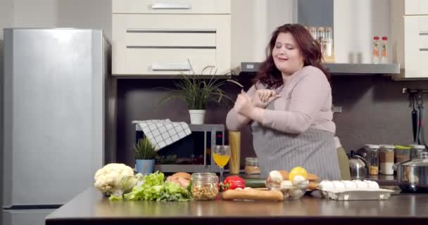 Attractive plus size young woman dancing energetic while cooking in kitchen. Body Positive concept — Stock Video