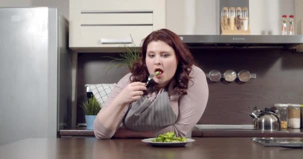 Mulher infeliz plus size comendo salada de legumes verdes na cozinha. Conceito de dieta, sobrepeso e alimentação saudável — Vídeo de Stock