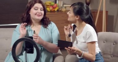 İki genç kadın güzellik ürünleri hakkında konuşuyor ve video kaydediyor ya da evde akıllı telefon kullanarak canlı yayın yapıyor. Güzellik, blog yazma ve sosyal medya kavramı