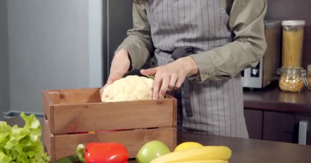 Mujer joven irreconocible sacando verduras frescas y frutas de una caja en la cocina. Entrega, comida orgánica y concepto de alimentación saludable — Vídeos de Stock