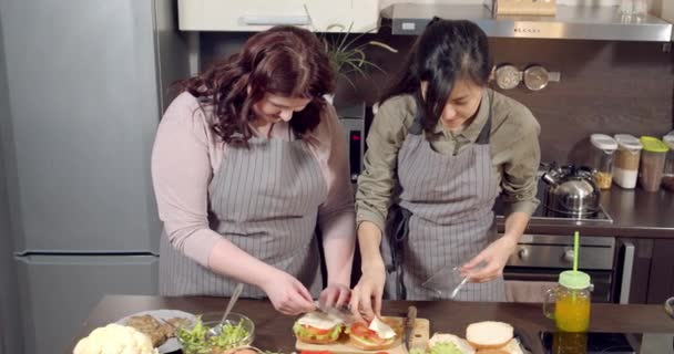 Deux jeunes femmes étalant des morceaux de fromage tout en préparant de délicieux hamburgers dans la cuisine — Video
