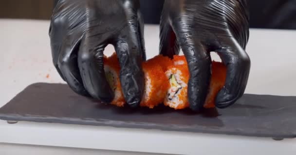 Close-up shot of a chef hands in black gloves serving delicious sushi with flying fish caviar on a plate — ストック動画