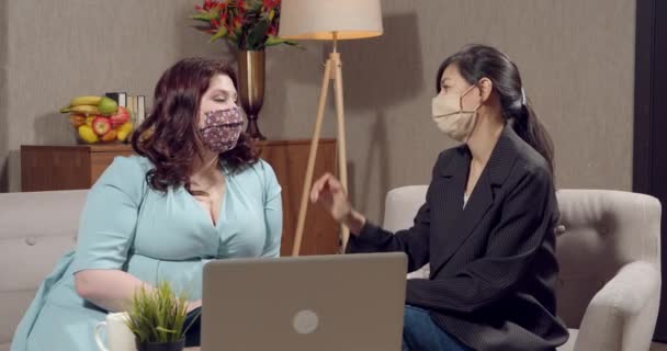 Two young women in protective masks discussing something and giving five in modern office. — Stock video