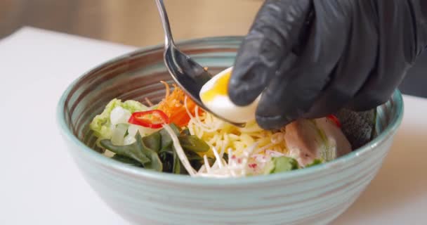 Zbliżenie rąk szefa kuchni w rękawiczkach przygotowujących pyszny ramen z kurczakiem, jajkiem i warzywami w kuchni. — Wideo stockowe