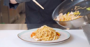 Eldivenli bir şefin yakın plan fotoğrafı. Lezzetli yumurtalı erişteyi tabağa deniz ürünleri koyarak.