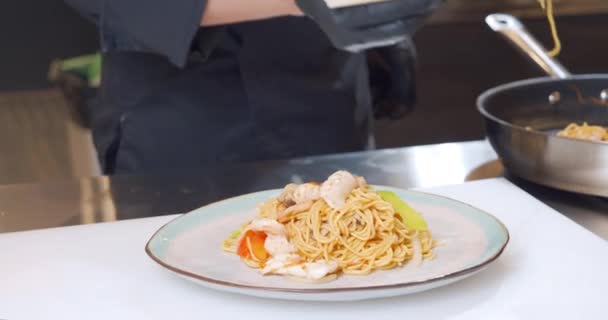 Primer plano de un chef manos en guantes poniendo deliciosos fideos de huevo con mariscos de una sartén en un plato — Vídeos de Stock