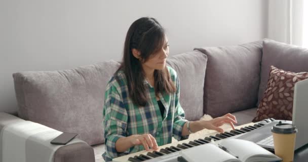 Jonge vrouw muziek leraar spelen elektrische piano onderwijs notities op afstand online met behulp van laptop tijdens het werken vanuit huis. — Stockvideo