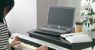 Evdeki dizüstü bilgisayarla çevrimiçi müzik öğrenirken tanınamayan bir kadının elektronik piyano çalarkenki yakın çekimi. 