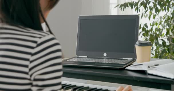 Крупный план неузнаваемой женщины, играющей на электронном пианино во время изучения музыки в Интернете с помощью ноутбука дома — стоковое видео