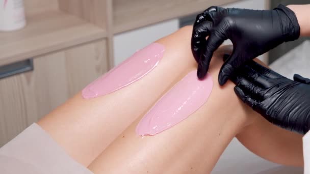 Primo piano di una donna estetiste mani in guanti rimuovere i capelli dalle gambe di un cliente femminile utilizzando cera cosmetica in un salone di bellezza. Procedura di depilazione. — Video Stock