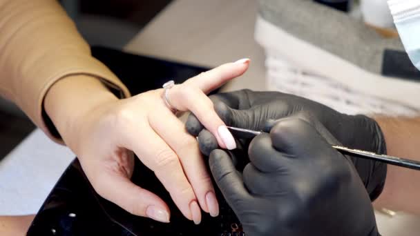 Primer plano de las manos de un maestro en guantes negros aplicando gel esmalte en las uñas de un cliente en un salón de belleza. Proceso de manicura. — Vídeos de Stock