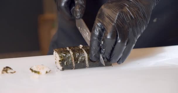 Primer plano de manos de chef masculino en guantes negros preparando deliciosos rollos de sushi con carne de cangrejo en la cocina. — Vídeo de stock