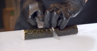 Erkek şefin yakın plan fotoğrafları. Siyah eldivenli elleri mutfakta yengeç etli suşi ruloları hazırlıyor..