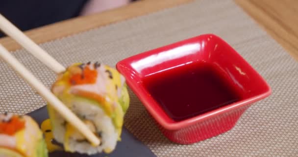 Close-up tiro de pauzinhos de bambu segurando delicioso rolo de sushi com salmão e abacate e mergulhando em uma tigela com molho de soja. — Vídeo de Stock
