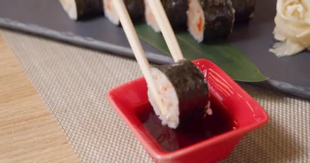 Close-up shot van bamboe eetstokjes met heerlijke sushi roll en dompelen in een kom met sojasaus. — Stockvideo