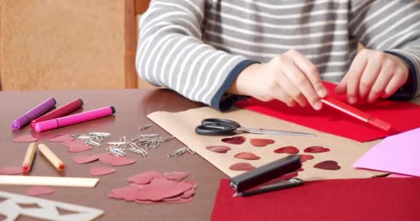 Primo piano di un bambino irriconoscibile che fa una cartolina fatta a mano da cuori rossi usando pennarelli multicolori e carta. Concetto di San Valentino — Video Stock