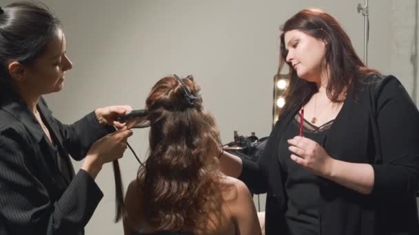 Professionele kapper en make-up kunstenaar doen kapsel en make-up aan een jonge vrouw klant in een schoonheidssalon. Concept van schoonheid en mode. Schieten in slow motion. — Stockvideo