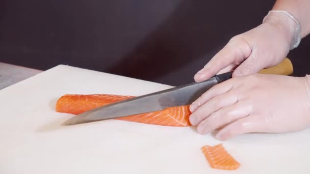 Primer plano manos de cocinero masculino en guantes de corte filete de salmón con cuchillo en pizarra blanca. — Vídeos de Stock