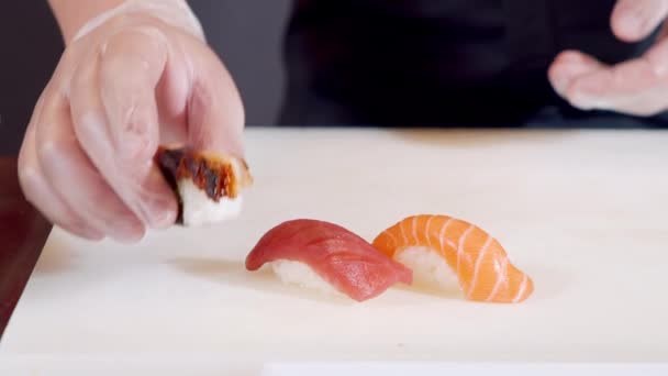 Primeros planos manos masculinas de cocinero en guantes poniendo sashimi con salmón y atún en un plato. — Vídeos de Stock