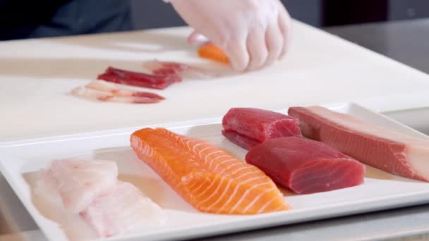 Κοντινό πλάνο με φέτες φρέσκου φιλέτου ψαριού σολομού, τόνου, lakedra και χταποδιού σε πιάτο. Αρσενικό χέρια σεφ σε γάντια προετοιμασία νόστιμα ορεκτικό του φρέσκου ψαριού — Αρχείο Βίντεο