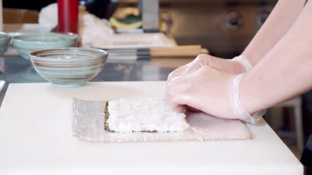 Закрыть руки шеф-повара в перчатках и приготовить суши-роллы на кухне — стоковое видео
