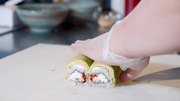Großaufnahme männlicher Kochhände in Handschuhen, die in der Küche köstliche Sushi-Rollen mit Avocado, fliegendem Fischrogen und Weichkäse zubereiten. — Stockvideo