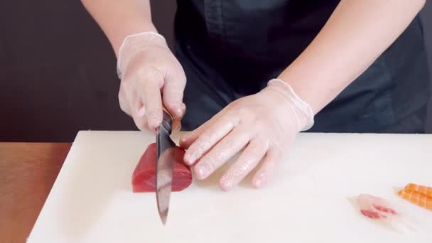 Männliche Kochhände in Großaufnahme in Handschuhen schneiden Thunfischfilet mit Messer auf weißem Brett. — Stockvideo
