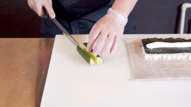 Primer plano de manos masculinas del chef en guantes rebanando pepino preparando rollos de sushi en la cocina — Vídeo de stock