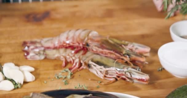 Närbild av matlagning av stora räkor med kryddor, salt, örter och vitlök på träskiva. Kockar händer i handskar tar skaldjur från bordet. — Stockvideo