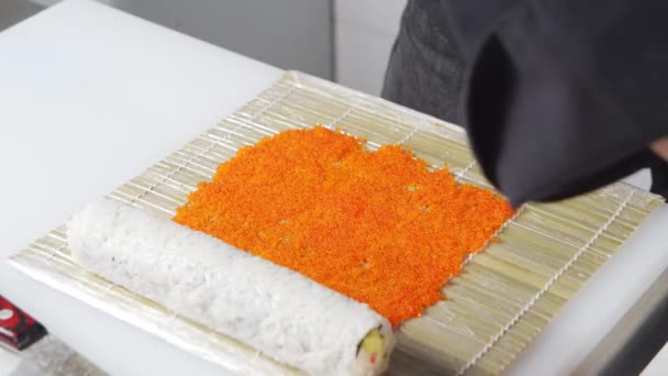 Close-up van mannelijke chef-kok handen in handschoenen bereiden sushi rollen met tobiko kaviaar in de keuken. — Stockvideo