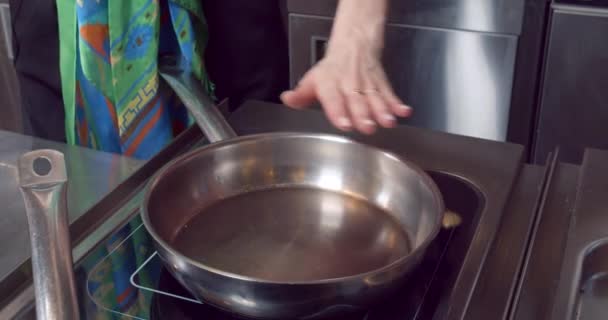Menutup tangan wanita memeriksa suhu penggorengan dan menuangkan minyak zaitun ke dalamnya di dapur — Stok Video