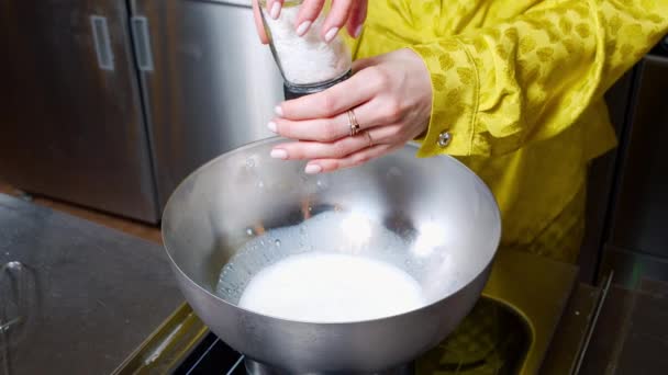 女性の手のクローズアップは、泡立て器で攪拌塩を追加し、暖かい牛乳の温度を確認します。カップケーキ生地を作る. — ストック動画