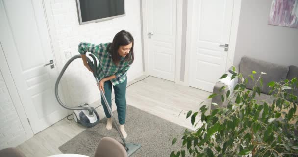 Jovem mulher limpeza de poeira e detritos de tapete cinza com aspirador de pó na sala de estar em casa. — Vídeo de Stock