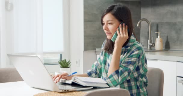 Młoda kobieta rozmawiająca przez komórkę pracująca na laptopie w biurze. Pracownica świadcząca profesjonalną poradę klientowi zdalnie korzystającemu z urządzeń bezprzewodowych. Praca na odległość. — Wideo stockowe