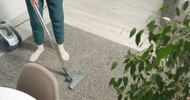 Evde elektrikli süpürge kullanarak gri halının tozunu ve enkazını temizleyen tanınmamış genç bir kadın.