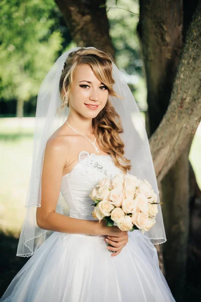 Bela noiva em vestido branco perto de uma árvore — Fotografia de Stock