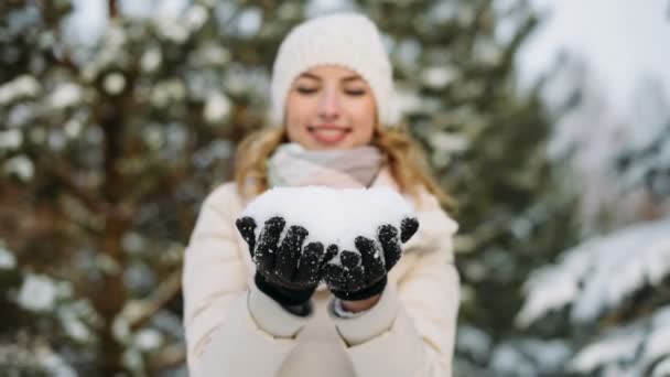 Vrouw in winter hoed blaast uit sneeuw uit handen — Stockvideo