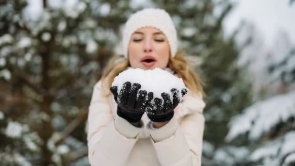 Mulher no chapéu de inverno sopra a neve das mãos — Vídeo de Stock