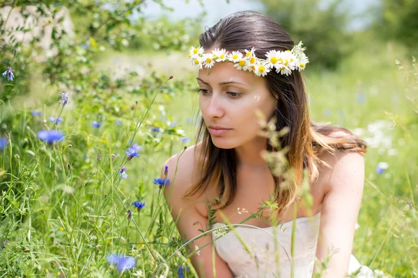 Jonge vrouw met een krans op haar hoofd onder bloemen veld — Stockfoto