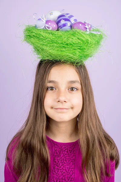 Klein meisje en nest met paaseieren over haar hoofd — Stockfoto