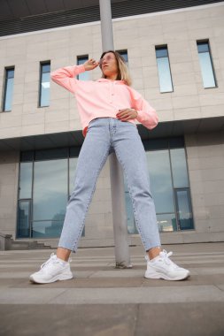 Güzel bir kadının dışarıdaki kameraya yakın çekimi. Spor kıyafetleriyle kameraya poz veren fitness kadını. Şehir caddesinde kapüşonlu kız portresi.