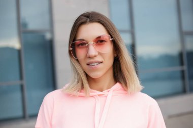 Güzel bir kadının dışarıdaki kameraya yakın çekimi. Spor kıyafetleriyle kameraya poz veren fitness kadını. Şehir caddesinde kapüşonlu kız portresi.