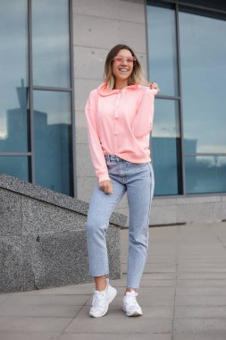 Güzel bir kadının dışarıdaki kameraya yakın çekimi. Spor kıyafetleriyle kameraya poz veren fitness kadını. Şehir caddesinde kapüşonlu kız portresi.