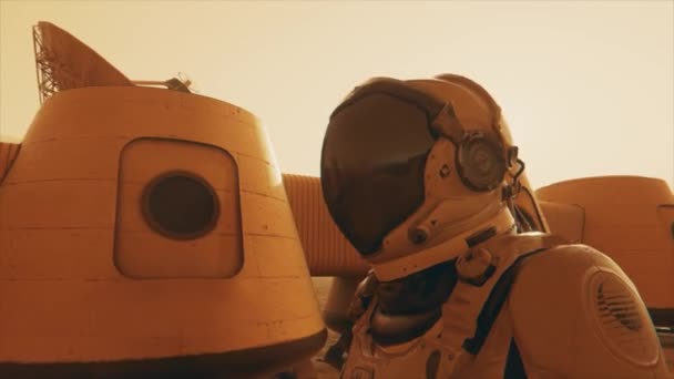 Űrhajós a Mars bolygón, kitérőt tesz a bázisa körül. Űrhajós sétál a bázison. Kis porvihar. A műholdantenna adatokat küld a földre. Realisztikus 3D animáció — Stock videók